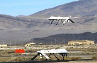 Two white drones flying over a field near mountains.