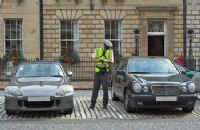 A man in yellow vest standing next to two cars.