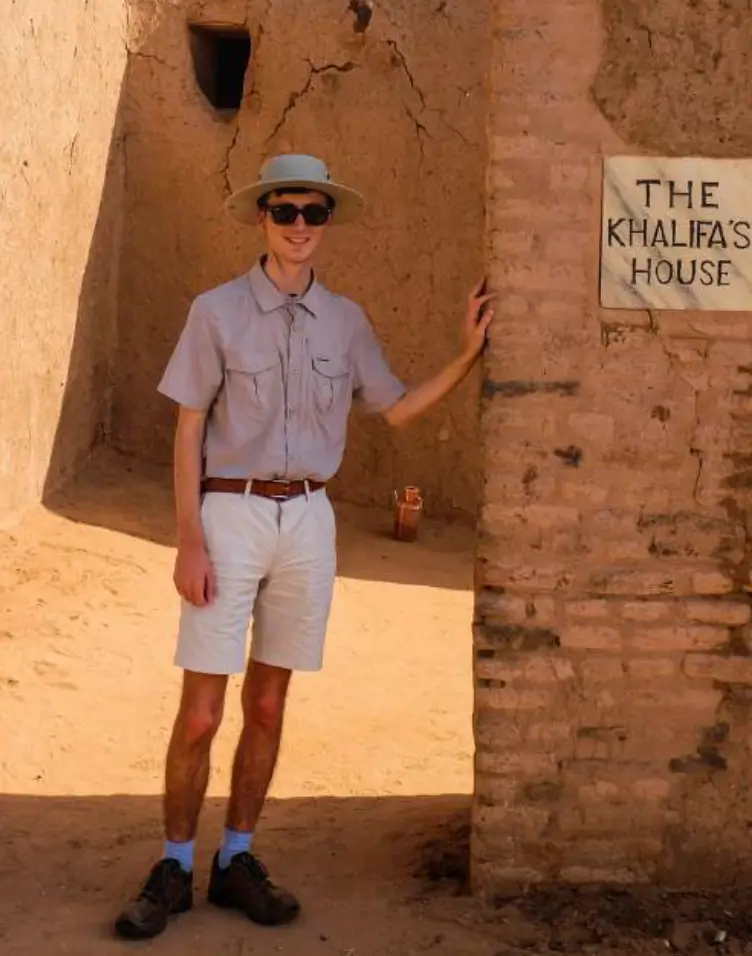 A man in shorts and hat standing next to a brick wall.